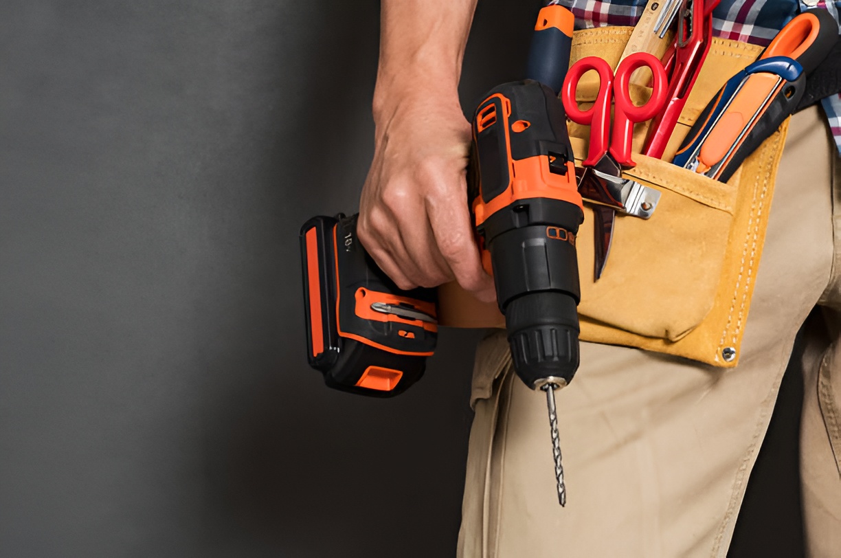 close-up of a man holding a drill and wearing a tool belt